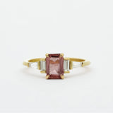 Gold ring with a Padparadscha pink sapphire and baguette diamonds on a white background