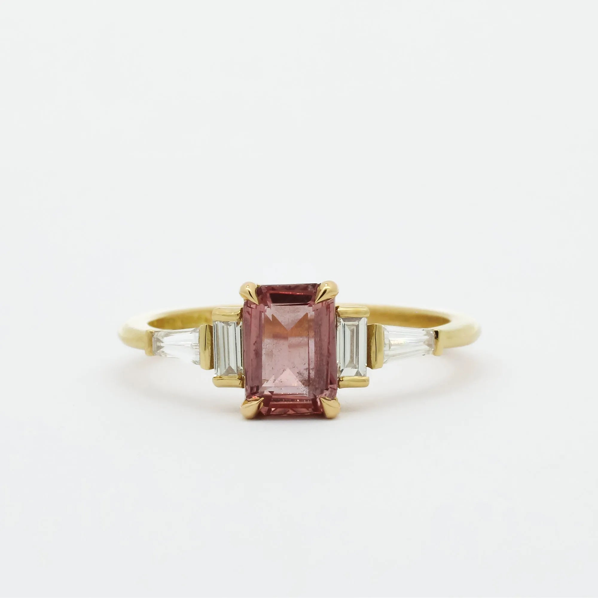 Gold ring with a Padparadscha pink sapphire and baguette diamonds on a white background