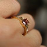 Close-up of a hand wearing a gold ring with a red gemstone on a blurred background