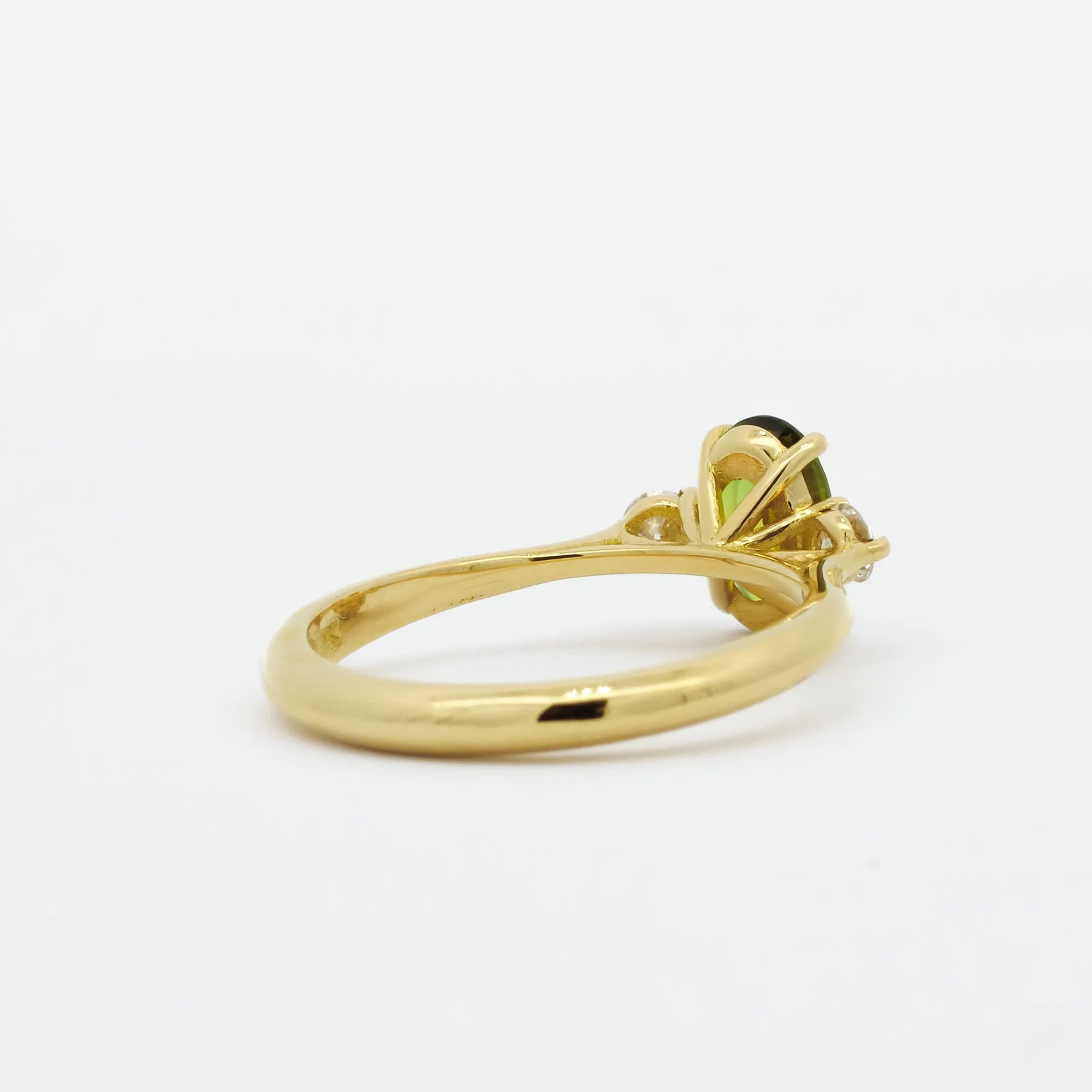 back view of gold engagement ring with a green gemstone on a white background