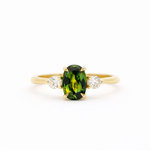 Gold trilogy engagement ring with an elongated green oval sapphire gemstone and two smaller diamonds on a white background