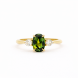 Gold trilogy engagement ring with an elongated green oval sapphire gemstone and two smaller diamonds on a white background
