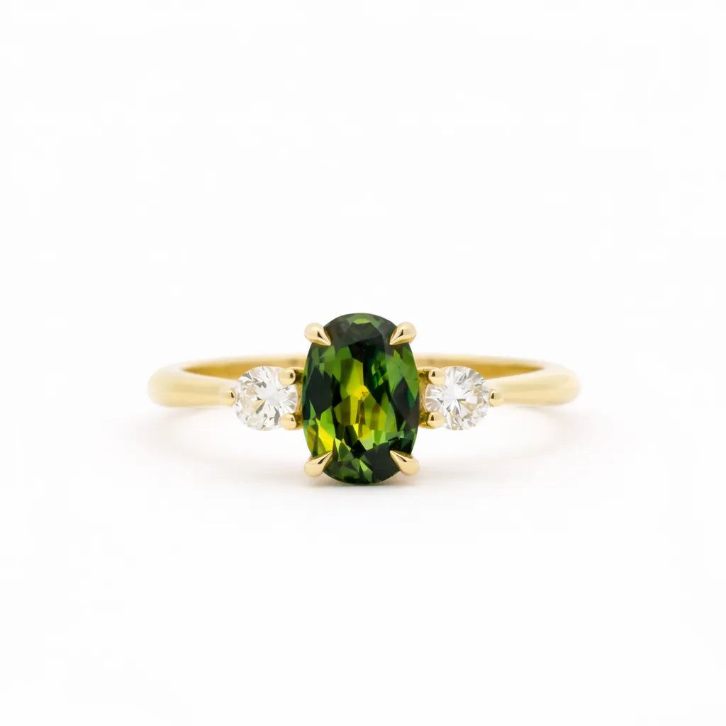 Gold trilogy engagement ring with an elongated green oval sapphire gemstone and two smaller diamonds on a white background