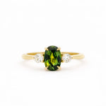 Gold trilogy engagement ring with an elongated green oval sapphire gemstone and two smaller diamonds on a white background