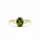 Gold trilogy engagement ring with an elongated green oval sapphire gemstone and two smaller diamonds on a white background
