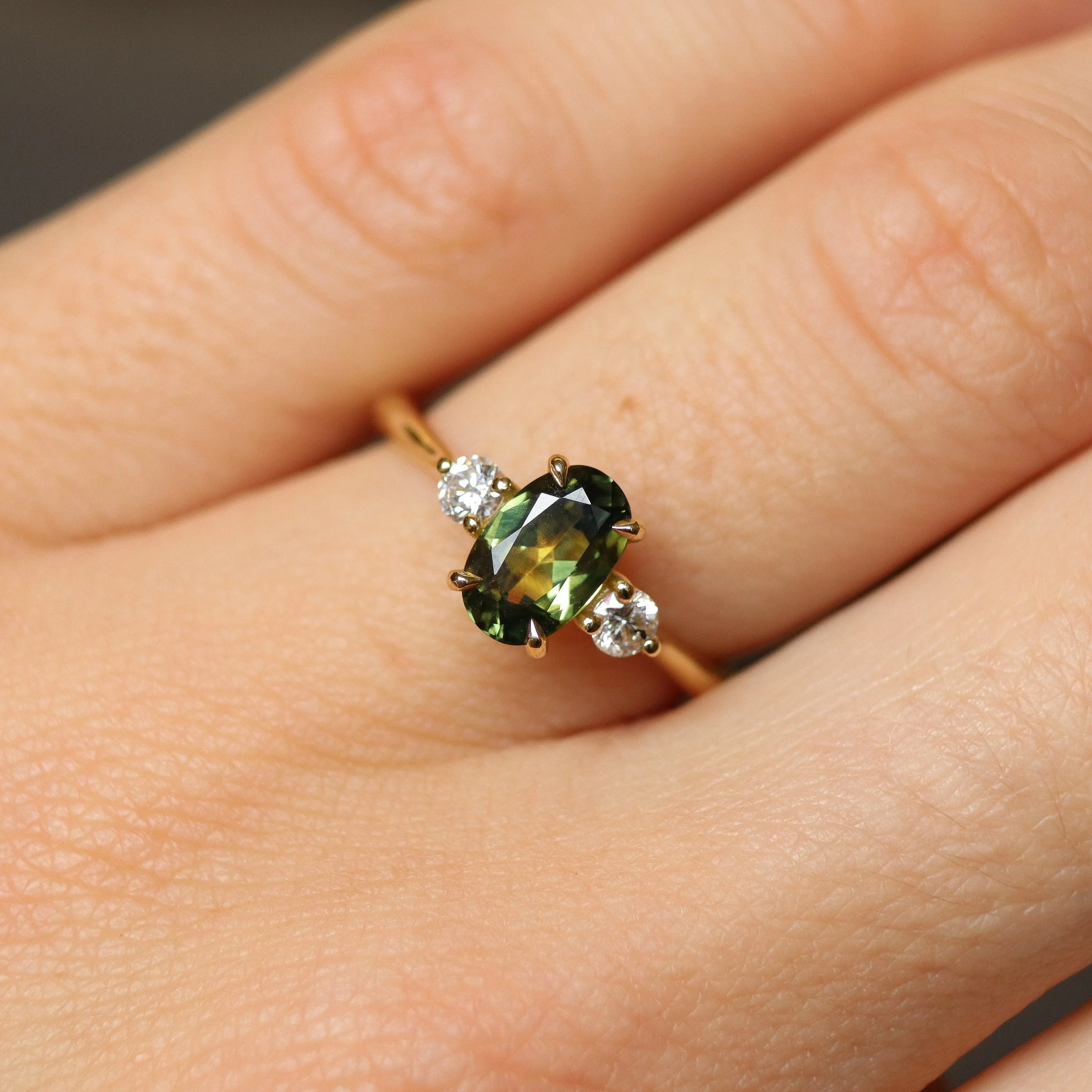 green and yellow engagement ring on finger