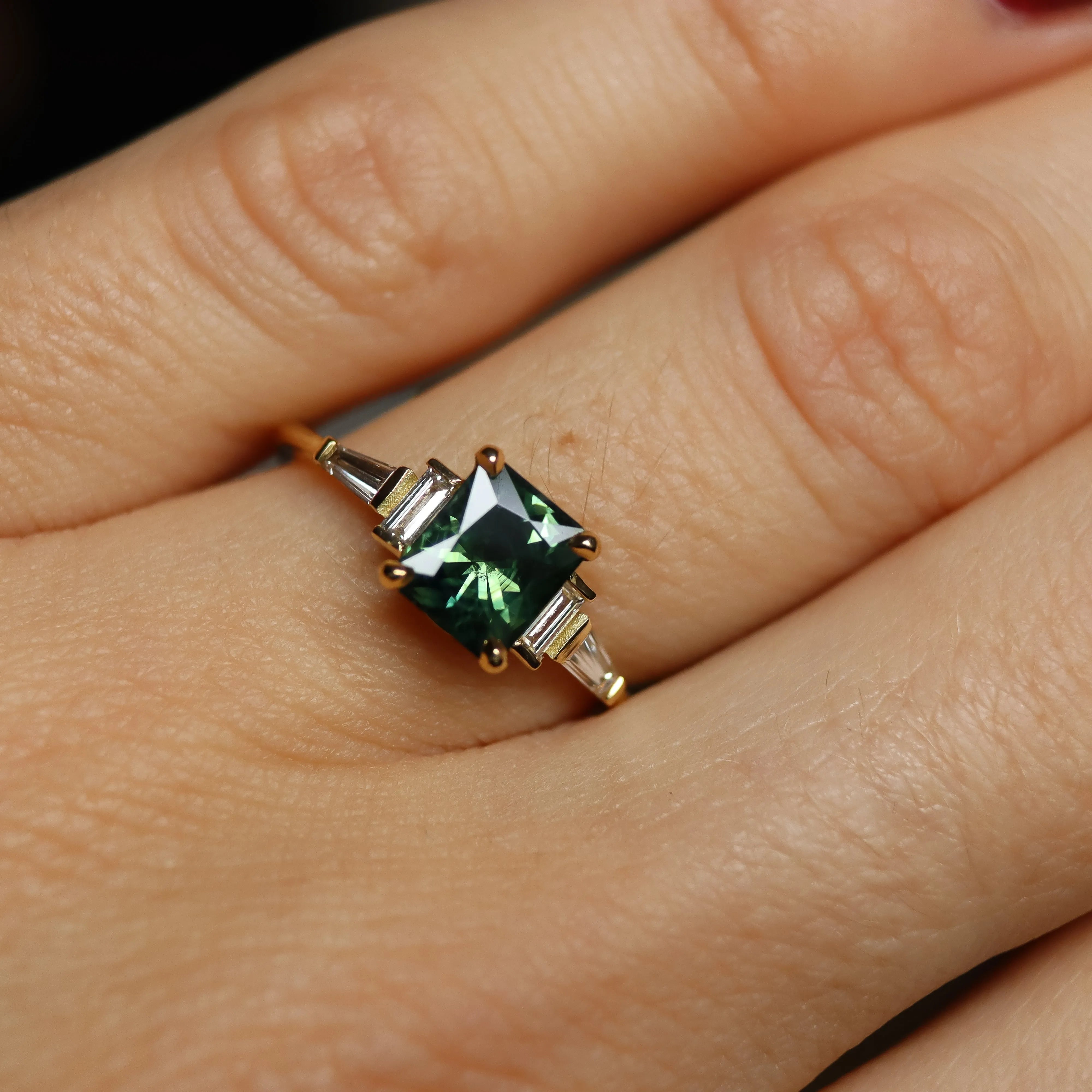 Gold ring with a green gemstone on a person's finger