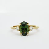 Gold ring with a slim oval sapphire gemstone and smaller diamonds on a white background