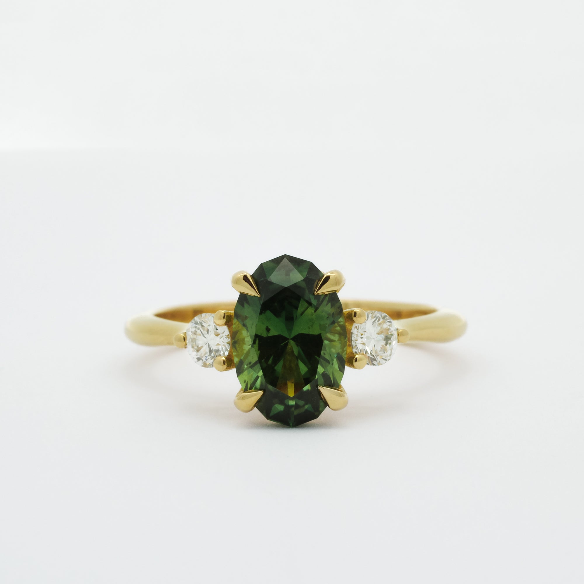 Gold ring with a slim oval sapphire gemstone and smaller diamonds on a white background