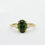 Gold ring with a slim oval sapphire gemstone and smaller diamonds on a white background