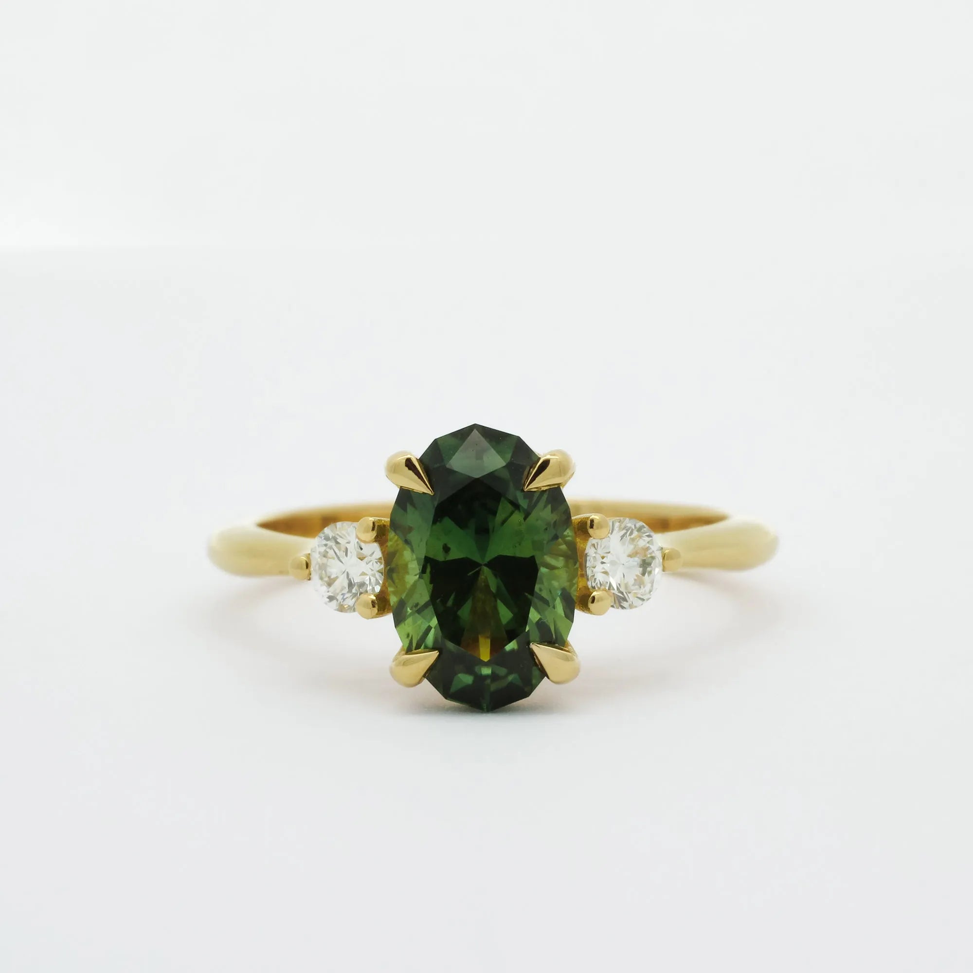 Gold ring with a slim oval sapphire gemstone and smaller diamonds on a white background