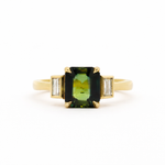 Gold ring with a green gemstone and smaller diamonds bezel set on a white background