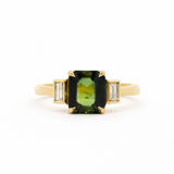 Gold ring with a green gemstone and smaller diamonds bezel set on a white background