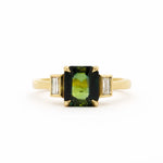 Gold ring with a green gemstone and smaller diamonds bezel set on a white background