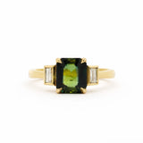 Gold ring with a green gemstone and smaller diamonds bezel set on a white background