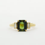 Gold ring with a green gemstone and smaller bezel diamonds on a white background