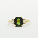 Gold ring with a green gemstone and smaller bezel diamonds on a white background