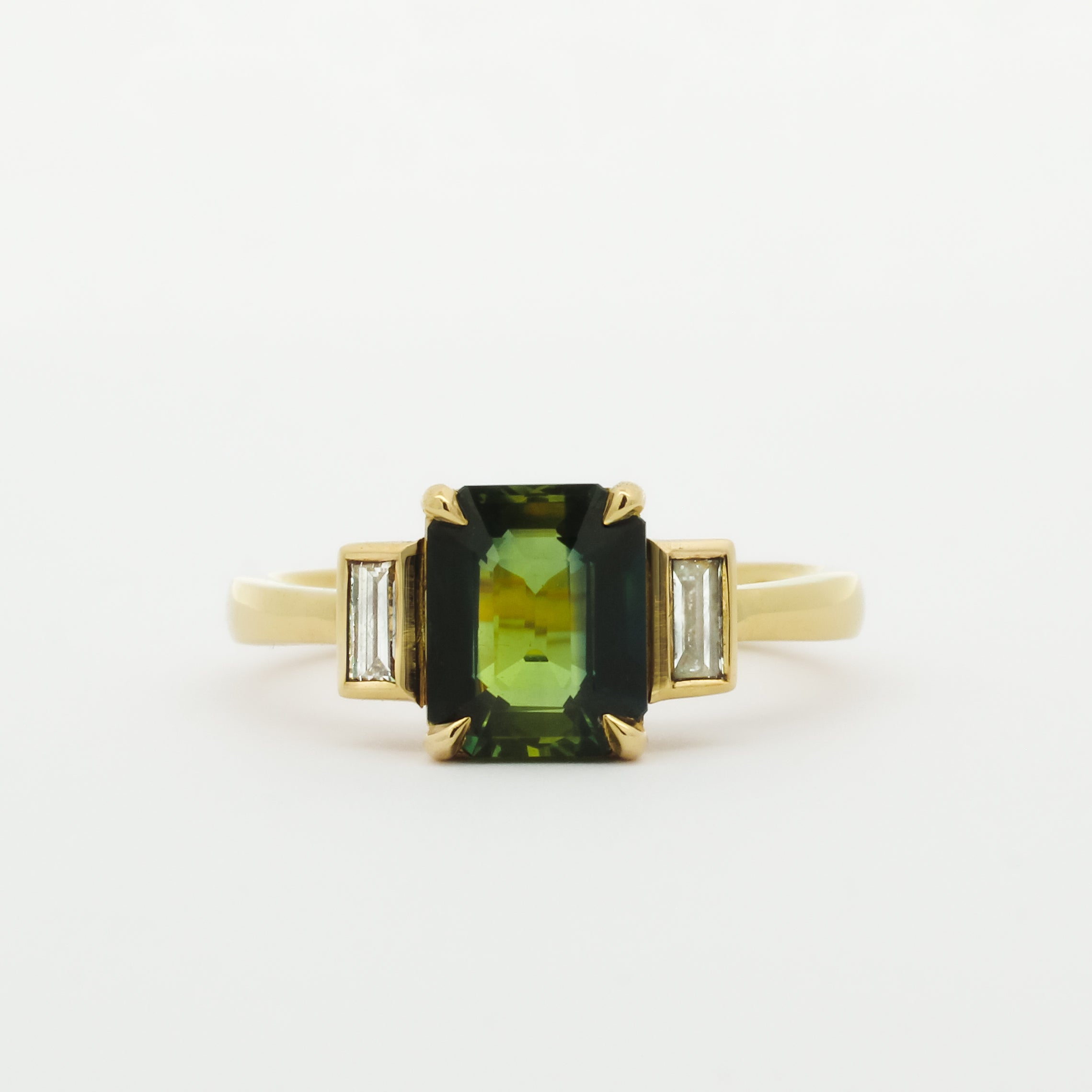 Gold ring with a green gemstone and smaller bezel diamonds on a white background
