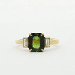 Gold ring with a green gemstone and smaller bezel diamonds on a white background