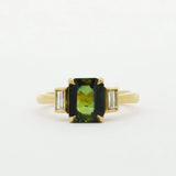Gold ring with a green gemstone and smaller bezel diamonds on a white background