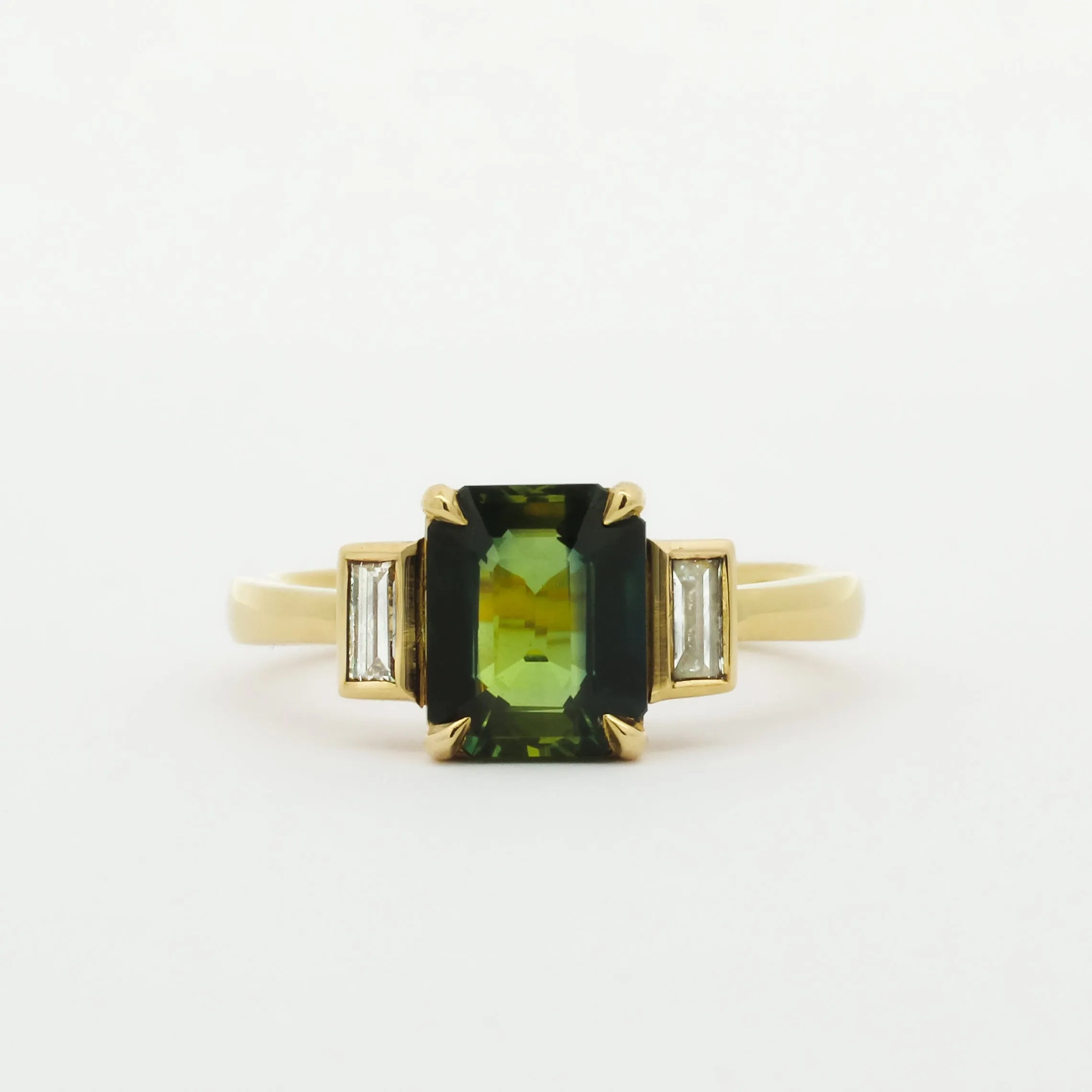 Gold ring with a green gemstone and smaller bezel diamonds on a white background