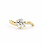 Gold engagement ring with waved shaped band with a round diamond on a white background