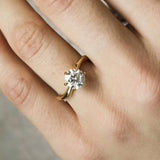 Gold ring with curved band and diamond on a hand against a neutral background