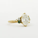 Gold engagement ring with a large diamond and smaller green gemstones on a white background