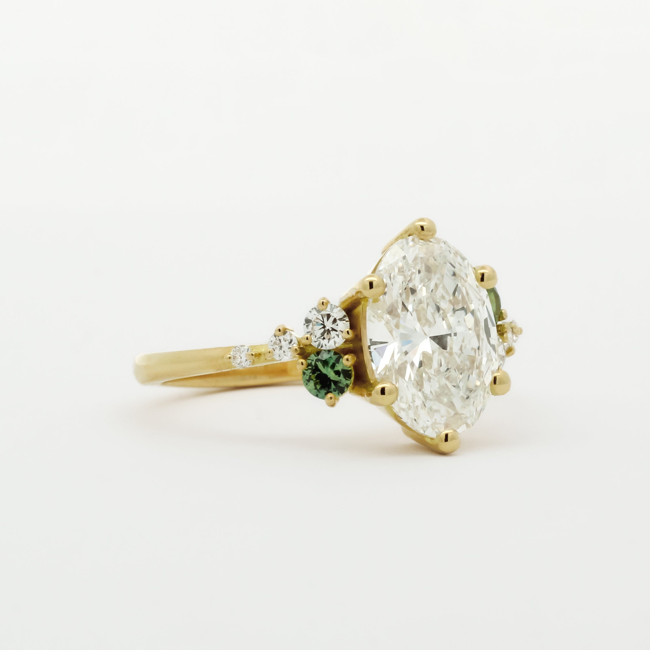 Gold engagement ring with a large diamond and smaller green gemstones on a white background