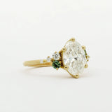 Gold engagement ring with a large diamond and smaller green gemstones on a white background