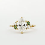 Gold ring with a large diamond and smaller green diamonds on a white background