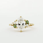 Gold ring with a large diamond and smaller green diamonds on a white background