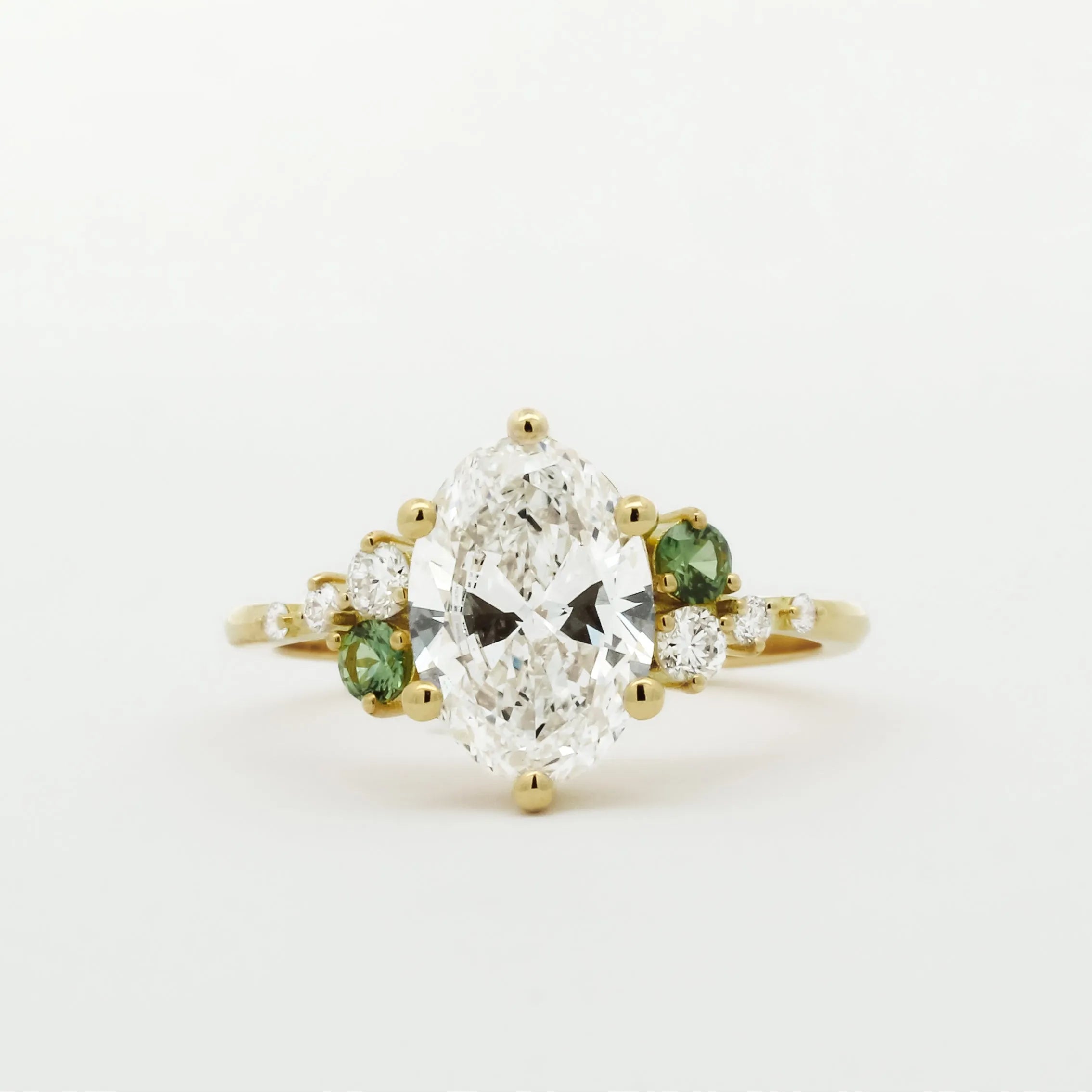 Gold ring with a large diamond and smaller green diamonds on a white background