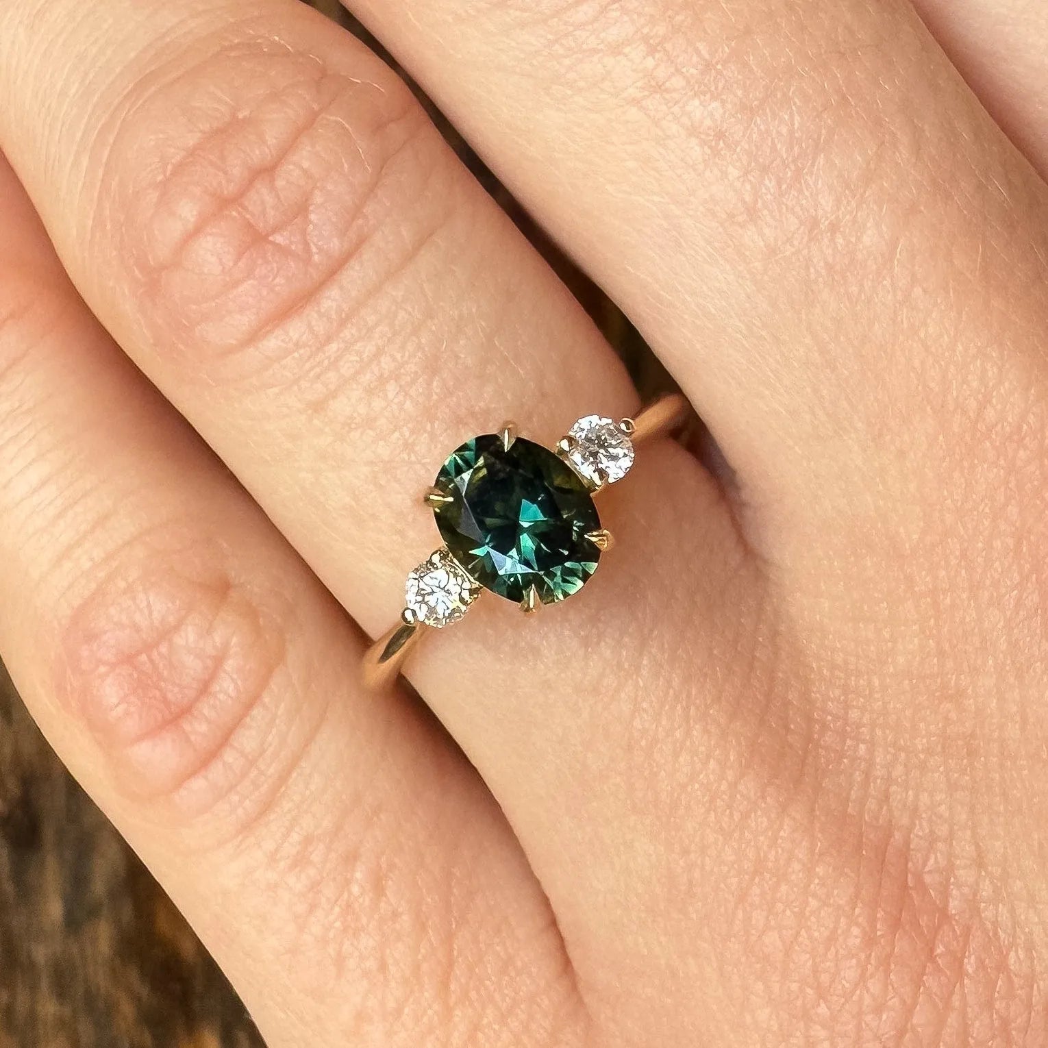 Close-up of a hand wearing an engagement ring with a green gemstone on a wooden surface