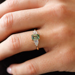 hand wearing green sapphire emerald-cut engagement ring with diamond cluster and gold band