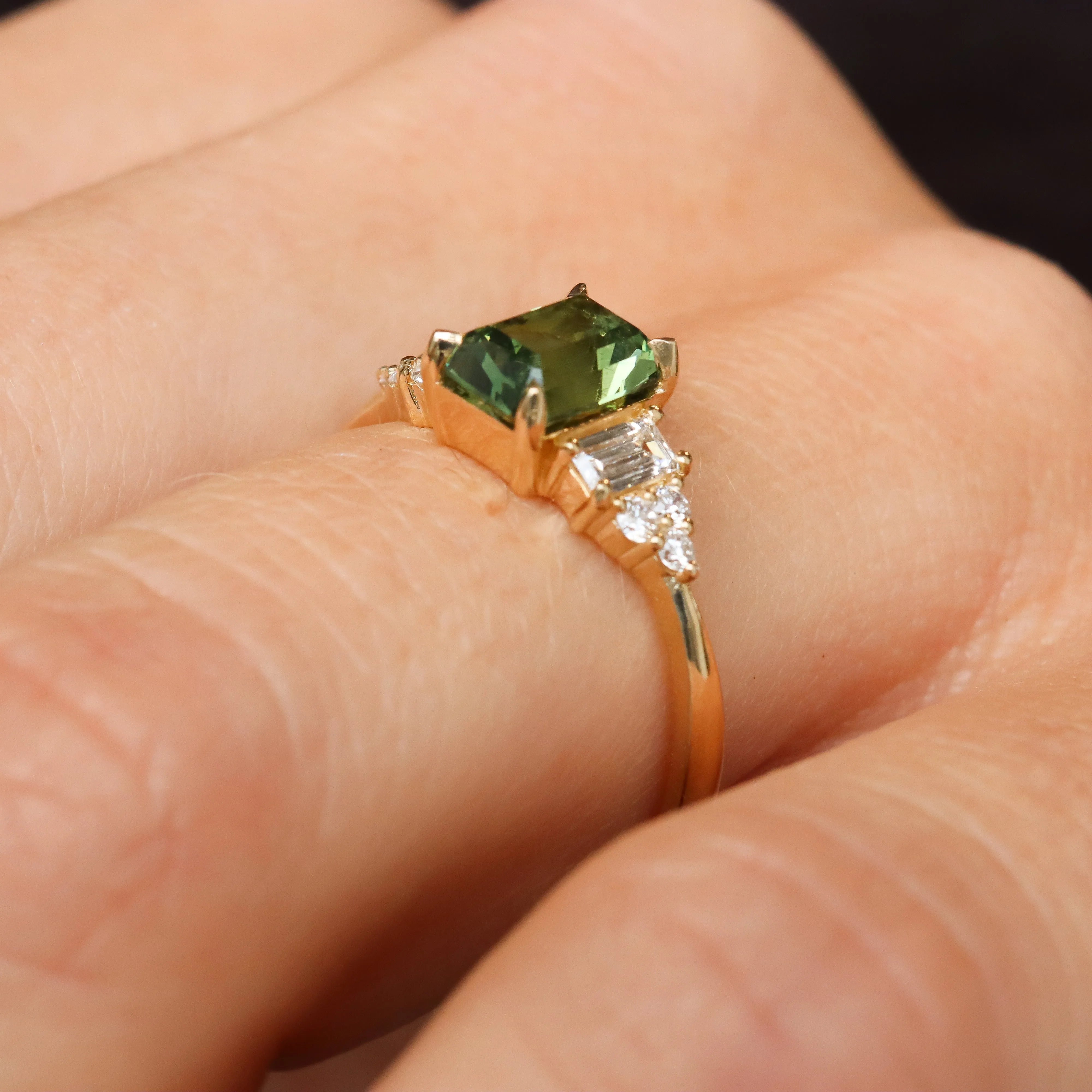 side profile of low set green sapphire diamond cluster engagement ring on finger