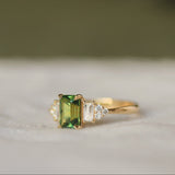 Gold emerald cut sapphire engagement ring with a green gemstone and diamonds on a textured surface