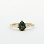 Gold ring with a green pear-shaped sapphire and smaller diamonds on a white background