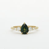 Gold ring with a green pear-shaped sapphire and smaller diamonds on a white background