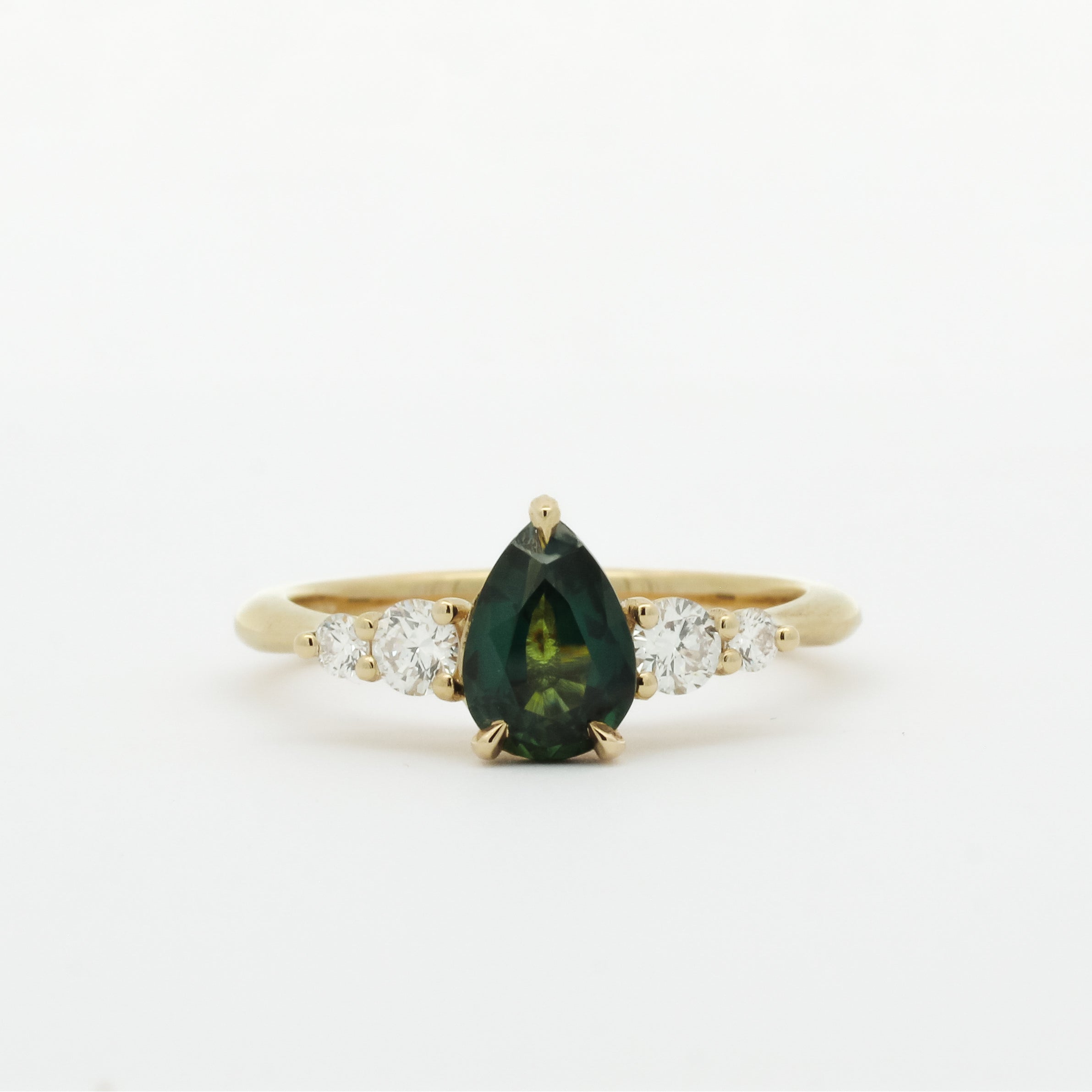 Gold ring with a green pear-shaped sapphire and smaller diamonds on a white background