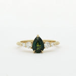 Gold ring with a green pear-shaped sapphire and smaller diamonds on a white background