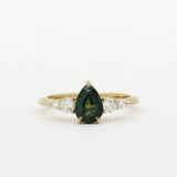 Gold ring with a green pear-shaped sapphire and smaller diamonds on a white background