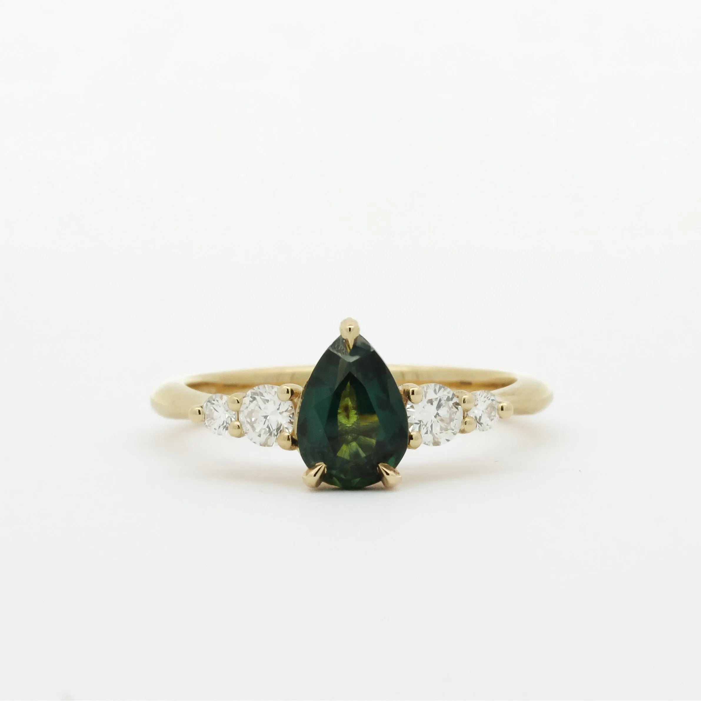 Gold ring with a green pear-shaped sapphire and smaller diamonds on a white background