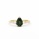 Gold ring with a green teardrop gemstone and smaller diamonds on a white background