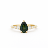 Gold ring with a green teardrop gemstone and smaller diamonds on a white background