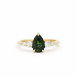 Gold ring with a green teardrop gemstone and smaller diamonds on a white background