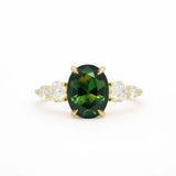 Ring with green oval sapphire, four round accent diamonds and gold claws on a white background