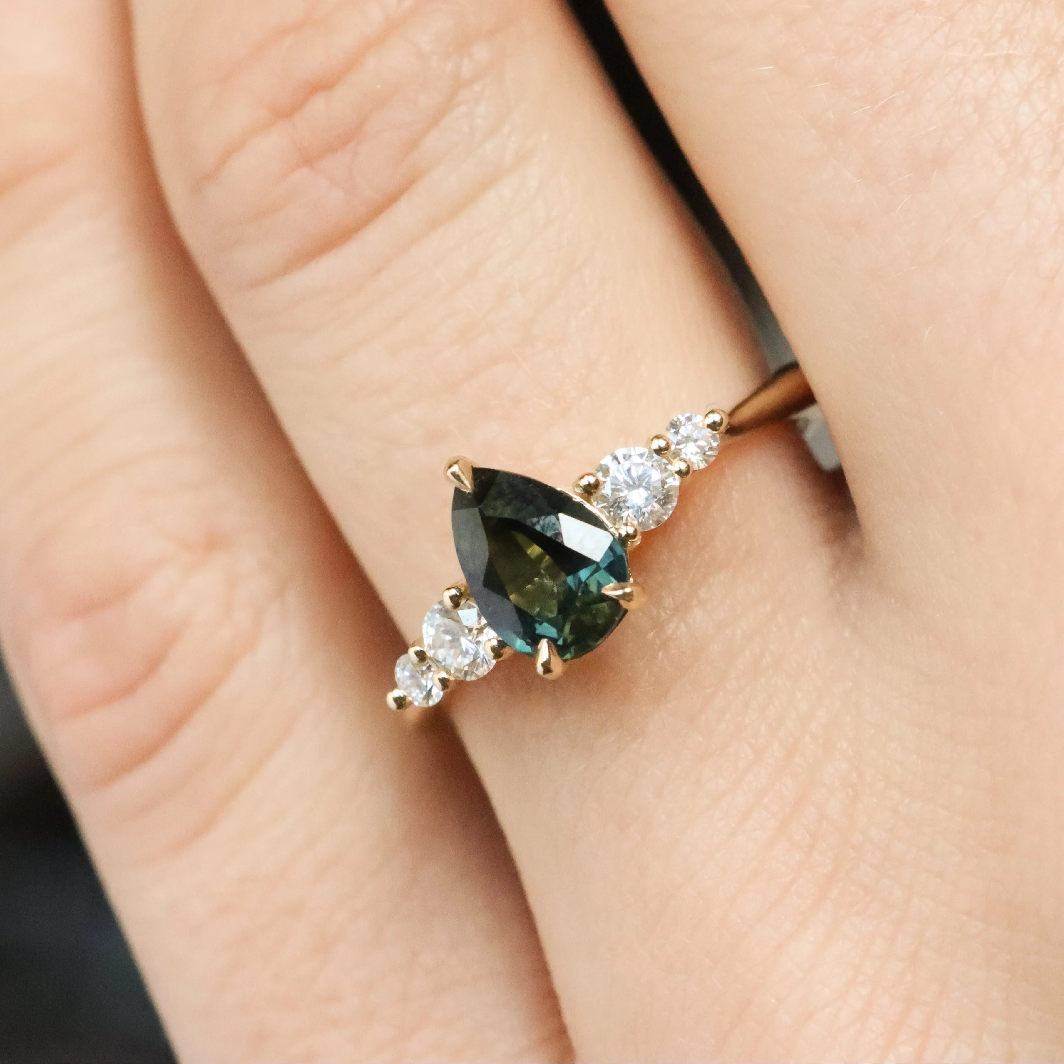 Ring with a green pear gemstone on a finger against a blurred background