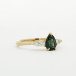 Gold engagement ring with a pear shaped green gemstone and smaller diamonds on a white background