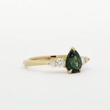 Gold engagement ring with a pear shaped green gemstone and smaller diamonds on a white background